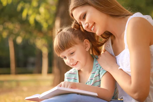 Vacker ung kvinna och hennes lilla dotter läser bok i parken — Stockfoto