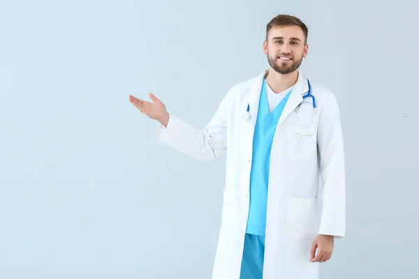 Portrait of male doctor showing something on light background — Stok fotoğraf