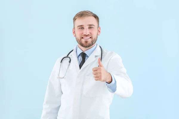 Portrait of male doctor showing thumb-up gesture on light background — Stock Photo, Image