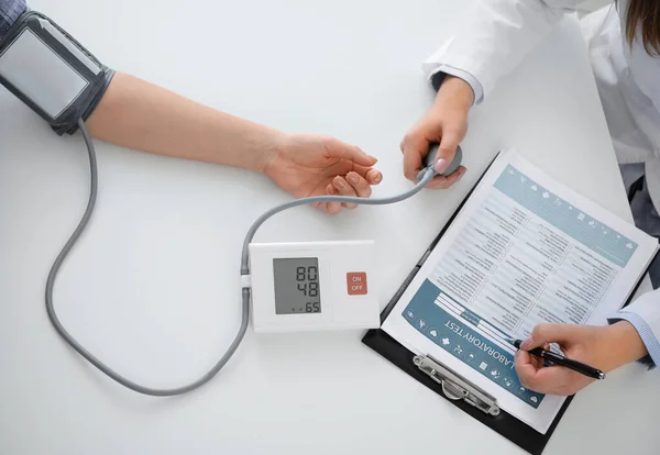 Médico que mide la presión arterial de la mujer en la clínica —  Fotos de Stock