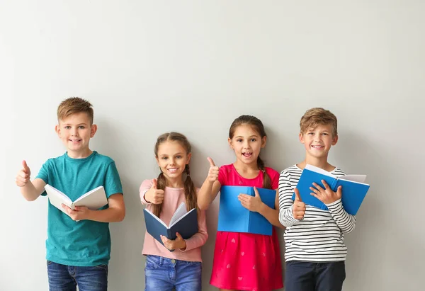 Schattige kleine kinderen met boeken met duim-up gebaar op grijze achtergrond — Stockfoto