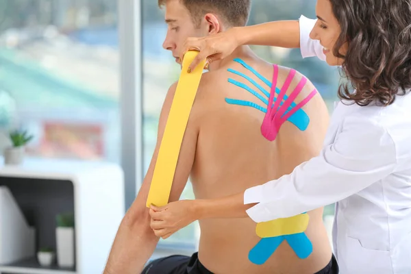 Fizjoterapeuta nakładający taśmę na męskie ramię w klinice — Zdjęcie stockowe