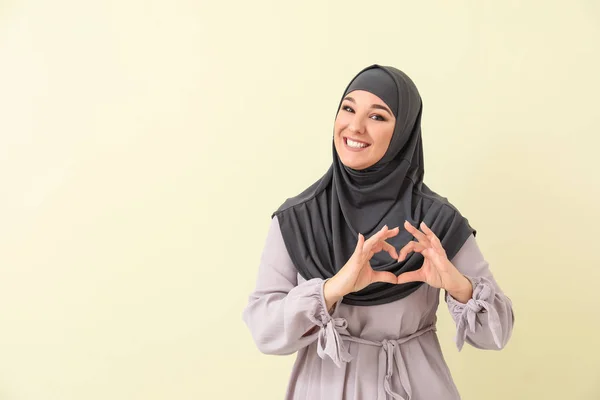 Beautiful young Muslim woman making heart with her hands on color background — ストック写真
