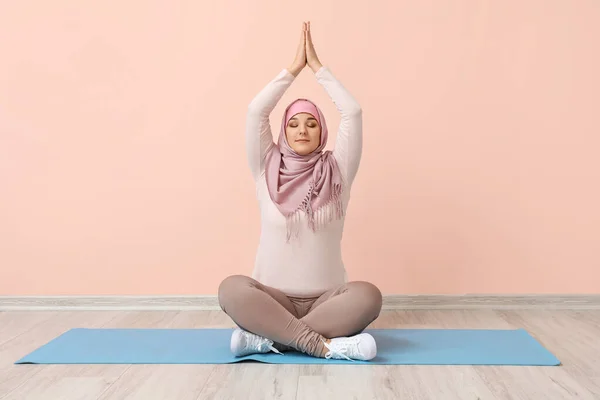 Mulher muçulmana desportiva praticando ioga perto da parede de cor — Fotografia de Stock