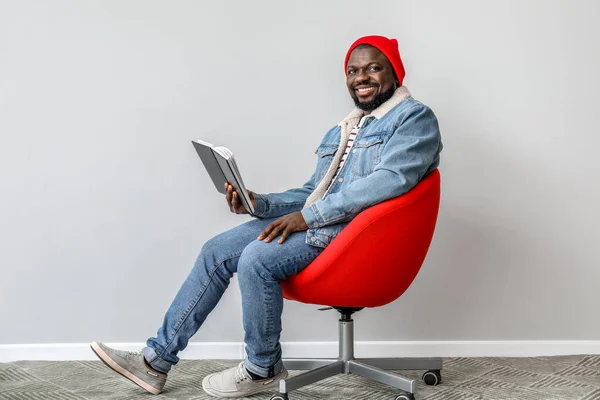 African-American man reading book near light wall — Stock Photo, Image