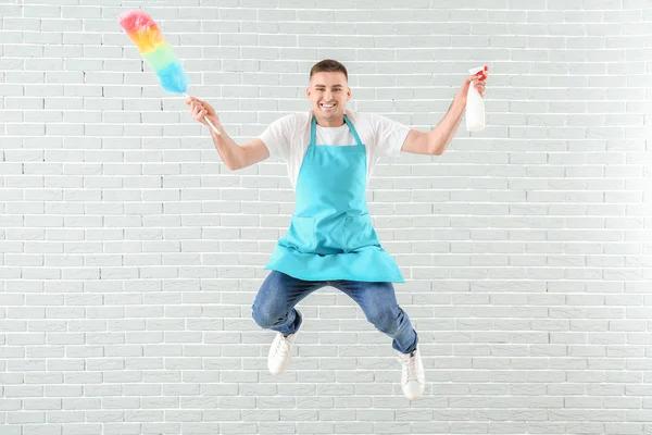 Jumping man with cleaning supplies against brick wall — 스톡 사진