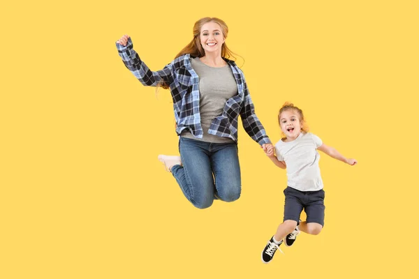 Jumping young woman and her little daughter on color background — Stock Photo, Image