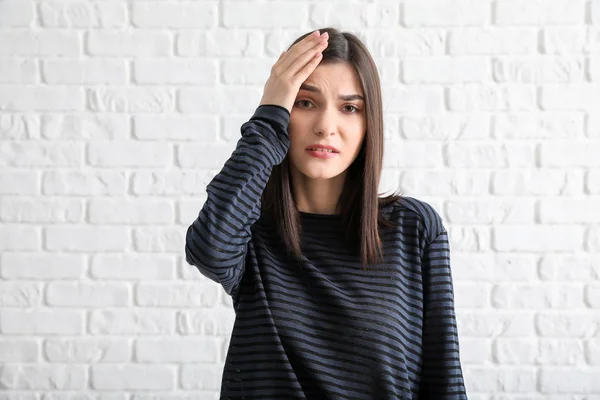 Worried young woman against white brick background — Stock Photo, Image