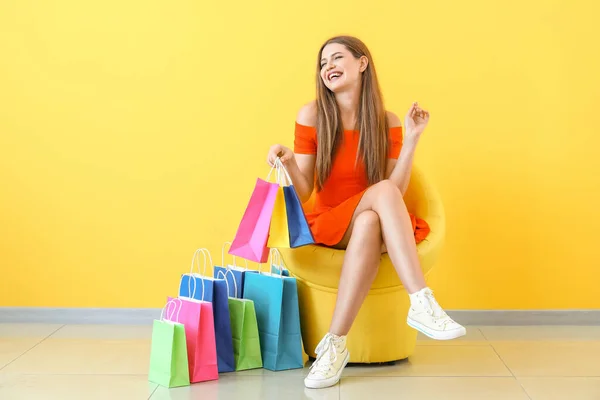 Mulher bonita com sacos de compras sentado em poltrona perto da parede de cor — Fotografia de Stock