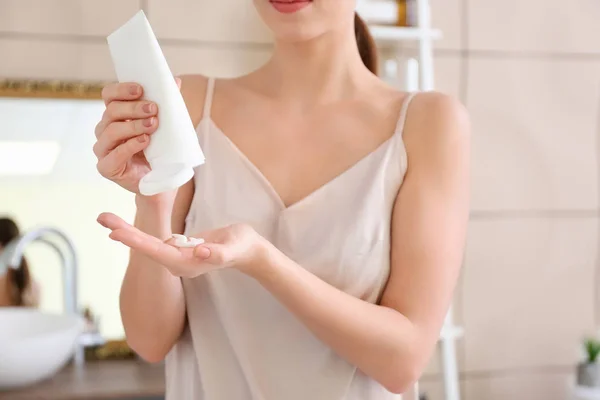 Beautiful young woman with tube of cream in bathroom — Stock Photo, Image