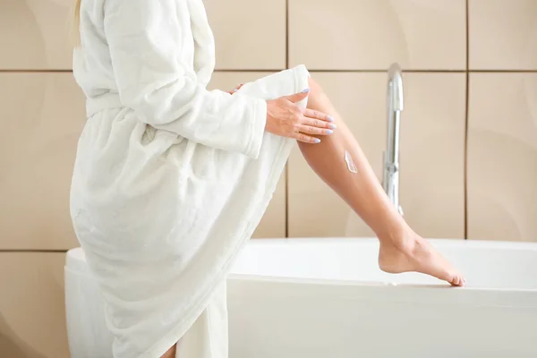 Hermosa mujer joven aplicando crema en su pierna en el baño — Foto de Stock