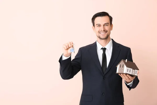 Männlicher Immobilienmakler mit Schlüssel und Modell des Hauses auf farbigem Hintergrund — Stockfoto
