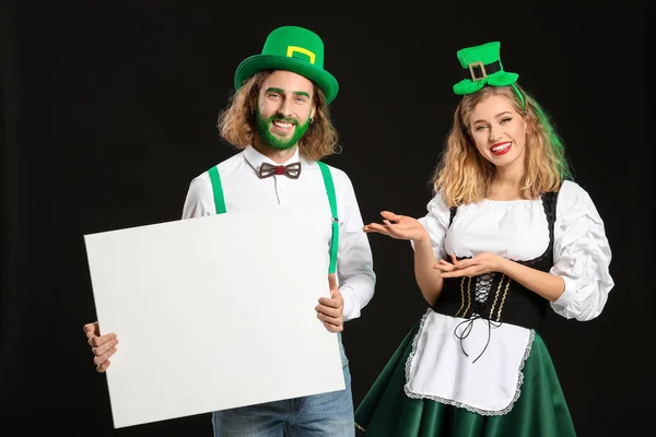 Young couple with blank poster on dark background. St. Patrick's Day celebration — Stock Photo, Image