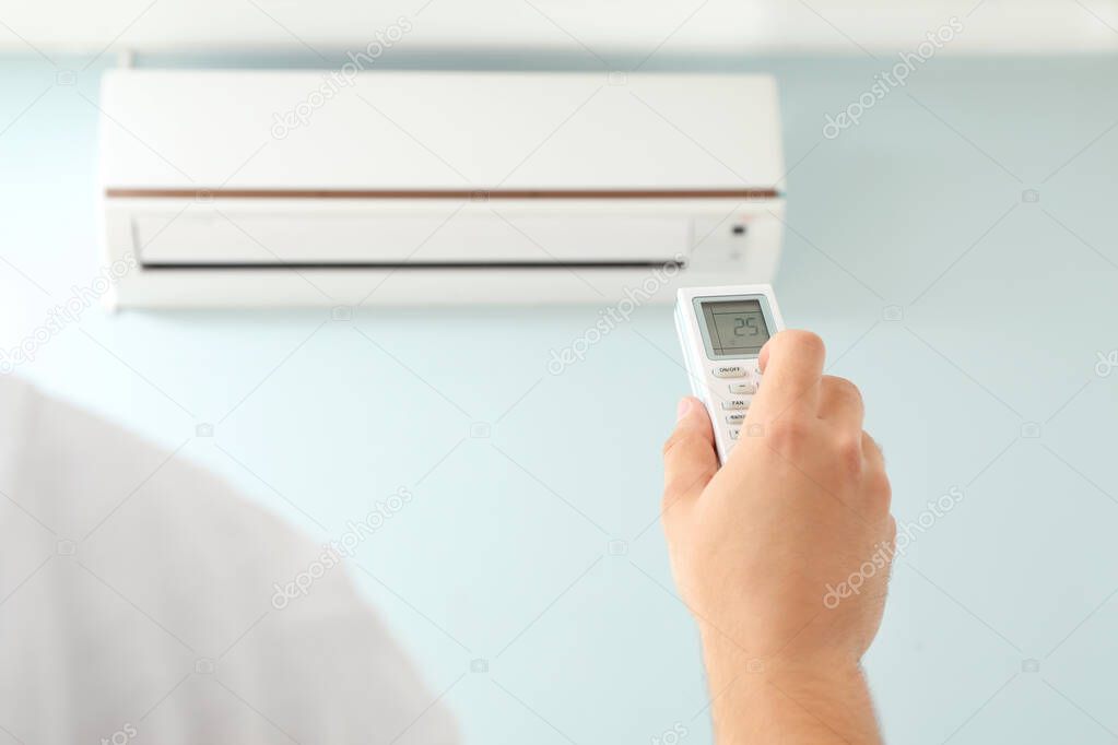 Young man switching on air conditioner at home