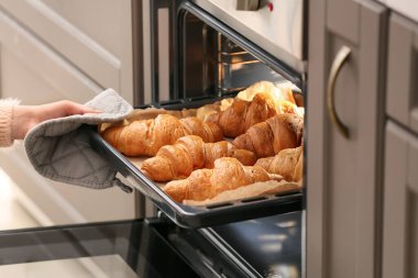 Fırından taze kruvasanla fırın tepsisi alan bir kadın.