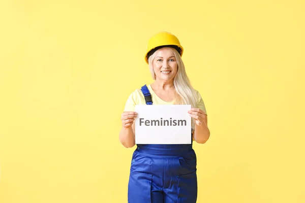女性労働者ホールド紙で単語フェミニズム上の色の背景 — ストック写真