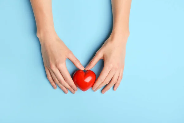 Жіночі руки з червоним серцем на кольоровому фоні. Концепція кардіології — стокове фото