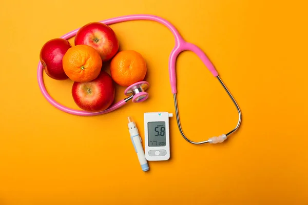 Glucosímetro digital, lápiz lanceta, estetoscopio y frutas sobre fondo de color. Concepto de diabetes — Foto de Stock