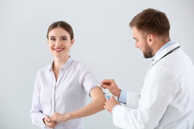 Doktor arka planda genç bir kadını aşılıyor.