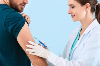 Doktor arka planda genç bir adamı aşılıyor.