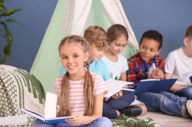 Cute little girl with friends reading books indoors