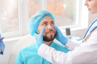 Klinikteki ameliyattan önce genç bir adamın yüzünü muayene eden estetik cerrah.
