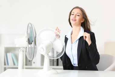 Ofiste sıcak hava dalgası sırasında elektrikli yelpaze kullanan genç bir kadın.