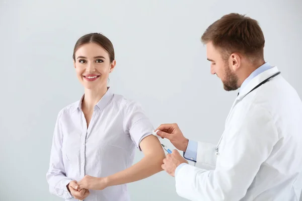 Doctor vaccinating young woman on light background — Stock Photo, Image