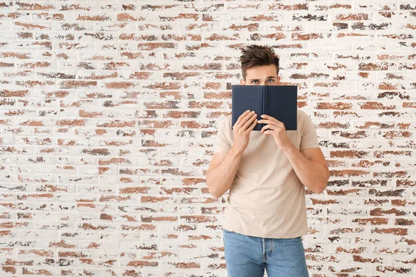 Przystojny młody człowiek z książką przy ceglanym murze — Zdjęcie stockowe