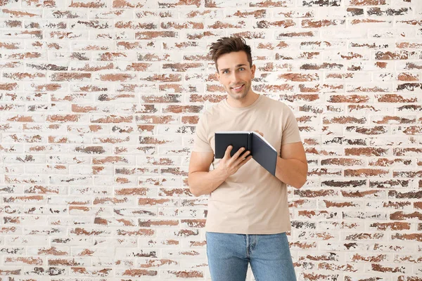 Schöner junger Mann mit Buch nahe Ziegelmauer — Stockfoto