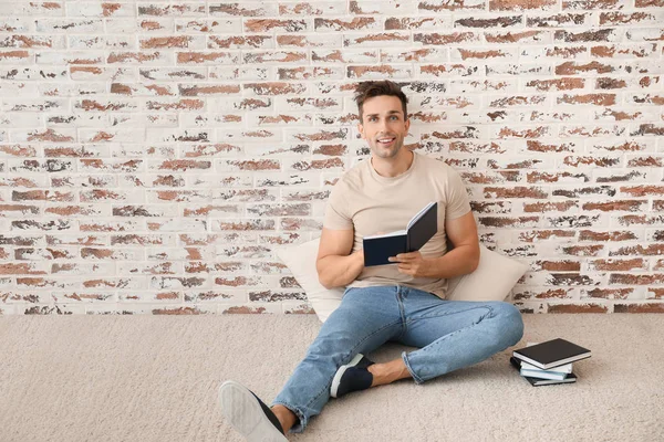 Handsome young man reading books near brick wall — Stock Photo, Image