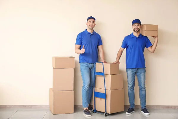 Delivery men with boxes near color wall — Stock Photo, Image
