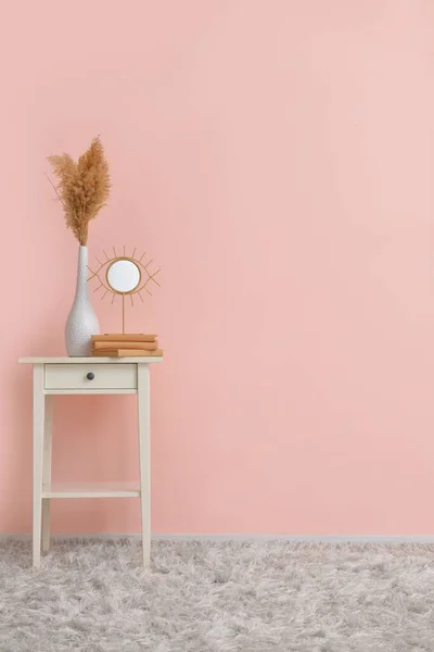 Table élégante avec vase, miroir et livres près du mur de couleur — Photo