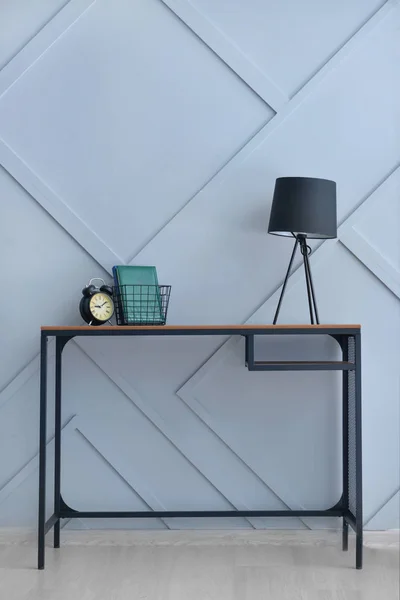 Стильный стол с лампой и будильником возле серой стены — стоковое фото