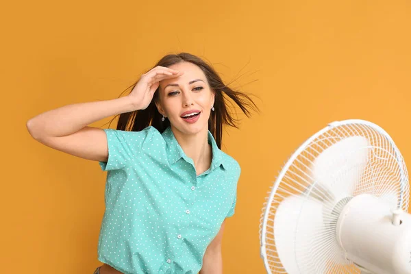 Young woman with electric fan on color background — Stock Photo, Image