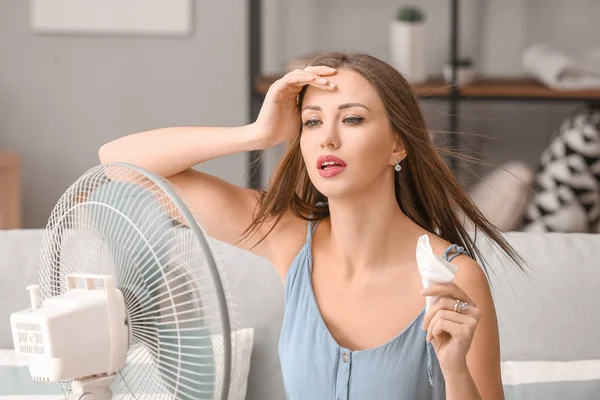 Young woman using electric fan during heatwave at home — Stock Photo, Image