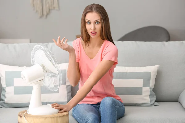Confused woman suffering from heat near electric fan at home — Stock Photo, Image