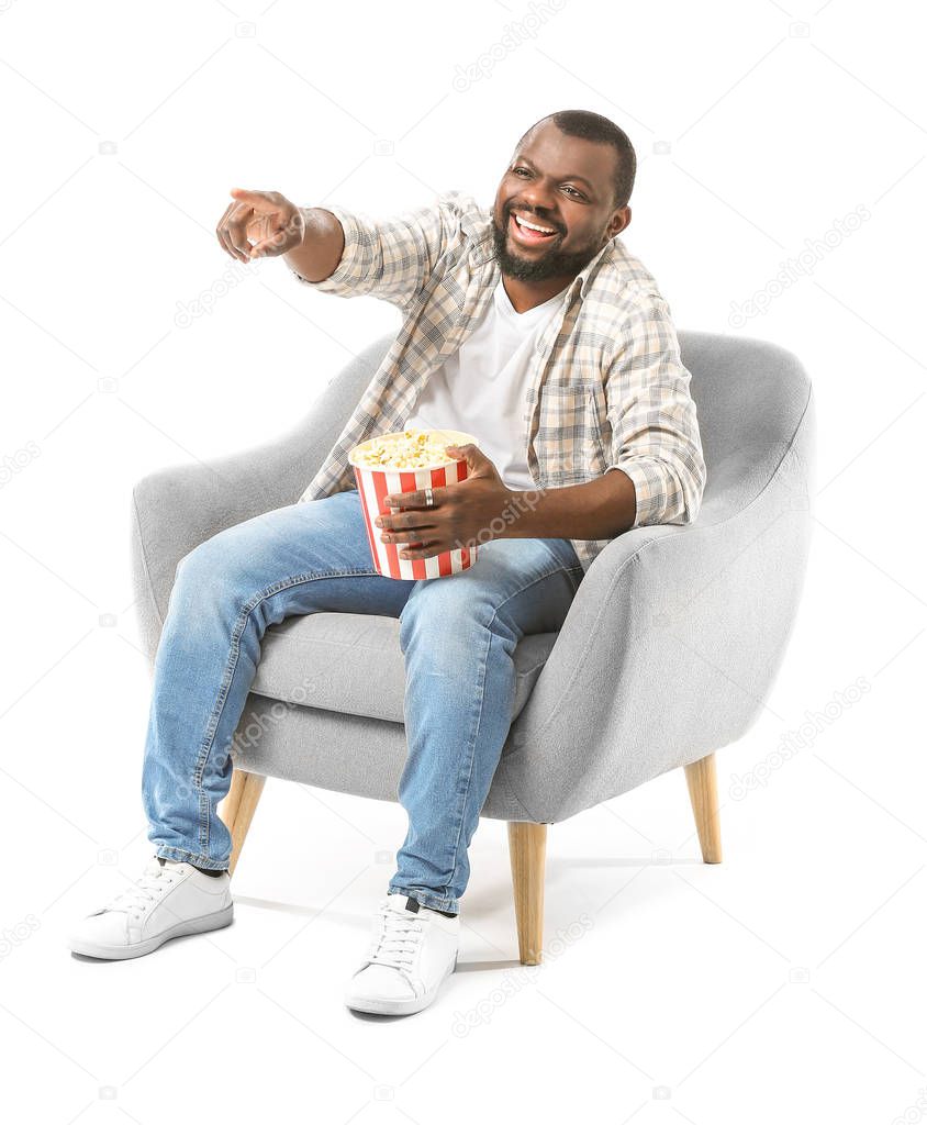 African-American man with popcorn watching TV while sitting in armchair against white background