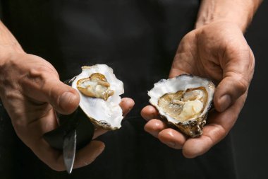 Koyu arkaplanda taze istiridye kabuğu açan adam.