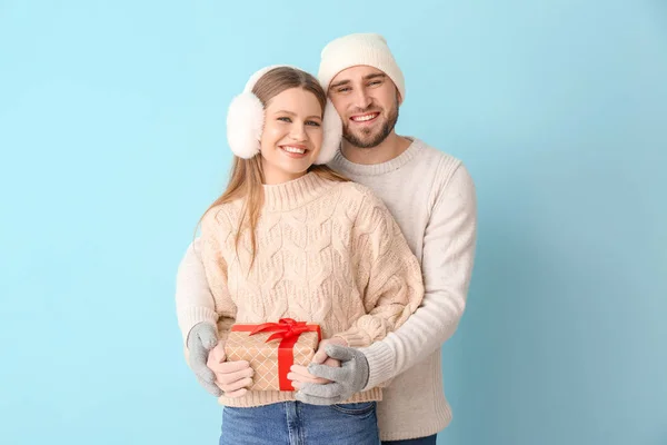 Retrato de pareja feliz en ropa de invierno y con regalo sobre fondo de color — Foto de Stock