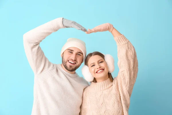 Retrato de pareja feliz en ropa de invierno haciendo forma de corazón con sus manos en el fondo de color — Foto de Stock