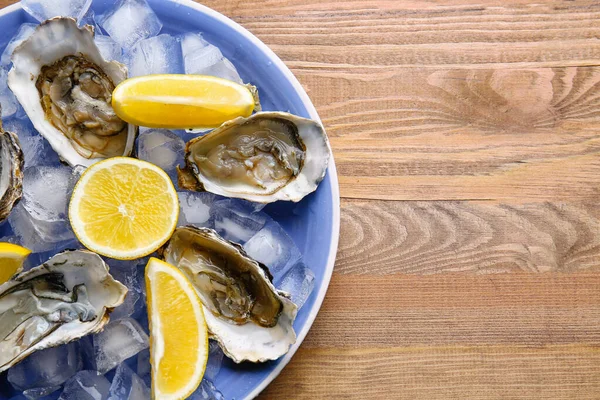 Tallrik med goda ostron, citron och is på bordet — Stockfoto