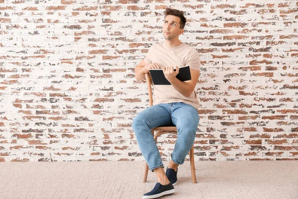 Handsome young man reading book near brick wall — Stock Photo, Image