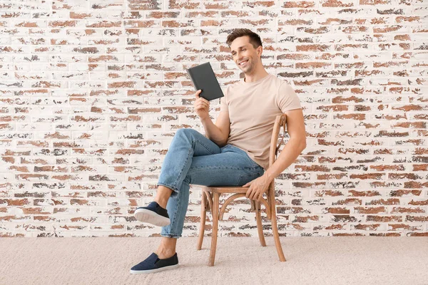 Handsome young man reading book near brick wall — Stock Photo, Image