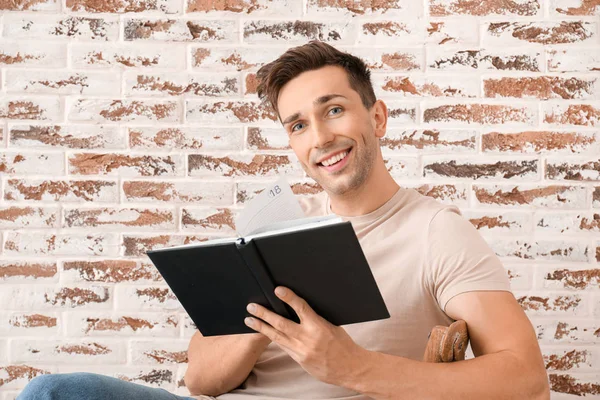 Przystojny młody człowiek czyta książkę przy ceglanym murze — Zdjęcie stockowe