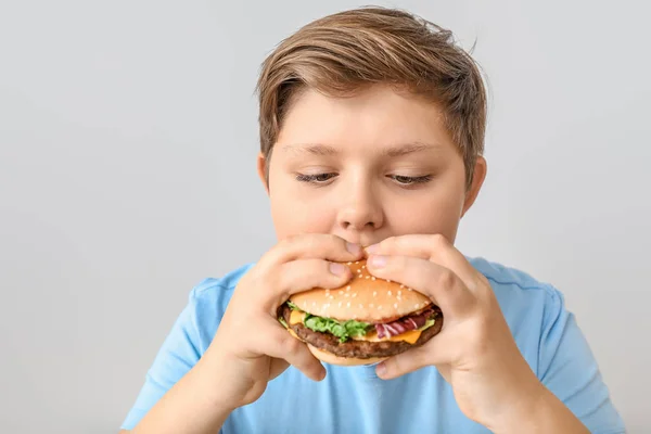 Niño con sobrepeso con hamburguesa sobre fondo claro — Foto de Stock