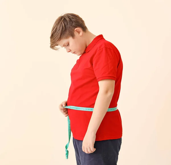 Overweight boy measuring his waist on light background — Stock Photo, Image