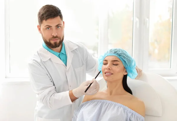 Plastic surgeon applying marks on patient's face in clinic — Stock Photo, Image