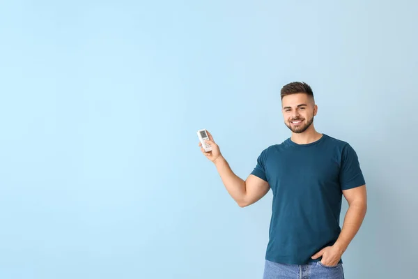 Young man with air conditioner remote control on color background — Stock Photo, Image