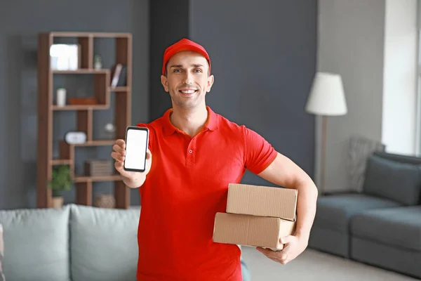 Handsome delivery man with boxes and mobile phone indoors — Stock Photo, Image